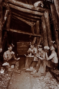 Photographie noir et blanc montrant quatre mineurs assis dans un boyau, en train de pique-niquer.