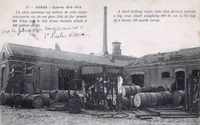 Carte postale noir et blanc montrant une usine détruite, entourée de gros tonneaux en métal renversés.