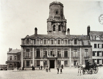 Photographie noir et blanc montrant la façade d'un imposant bâtiment. À l'arrière une tour se détache.