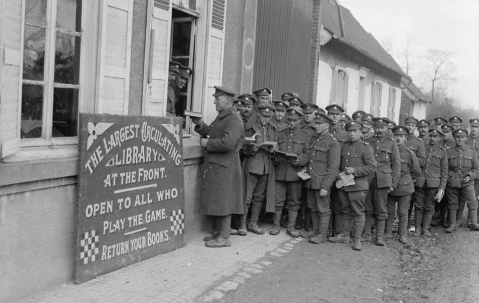 Photographie noir et blanc montrant une queue deavtn les fenêtres d'une maison ouverte. À côté, un panneau écrit en anglais indique qu'il s'agit d'une librairie.