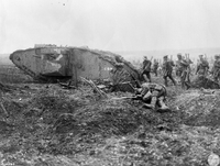 Photographie noir et blanc montrant des soldats marchant derrière un tank. Au premier plan, un soldat mort.