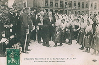 Carte postale noir et blanc montrant un homme, entouré d'une délégation officielle, en train de serrer la main à une femme en habit traditionnel de matelote.