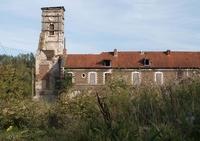 Photographie couleur montrant le campanile d'une église suivie de longs bâtiments.