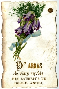 Carte postale couleur représentant une gerbe de fleurs violettes ceinte d'un ruban bleu ciel. En-dessous, on lit "d'Arras je vous envoie mes souhaits de bonne année". Sur le côté est rajoutée une mention manuscrite "Voeux sincères. Marie-Thérèse. 3 janvier 1908".