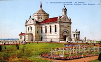 Carte postale couleur montrant un édifice religieux entouré de tombes représentées par des croix blanches.