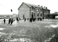 Photographie noir et blanc montrant des élèves faisant une partie de football dans la cour d'une école.