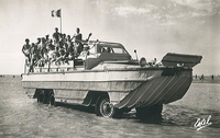 Photographie noir et blanc montrant un groupe de personnes dans un camion-amphibie sur une plage.