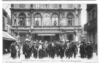Carte postale noir et blanc montrant un groupe de personnes sortant d'un grand bâtiment paré de drapeaux et sur lequel a été apposé une pancarte où l'on distingue écrit écrit "L'esperanto".