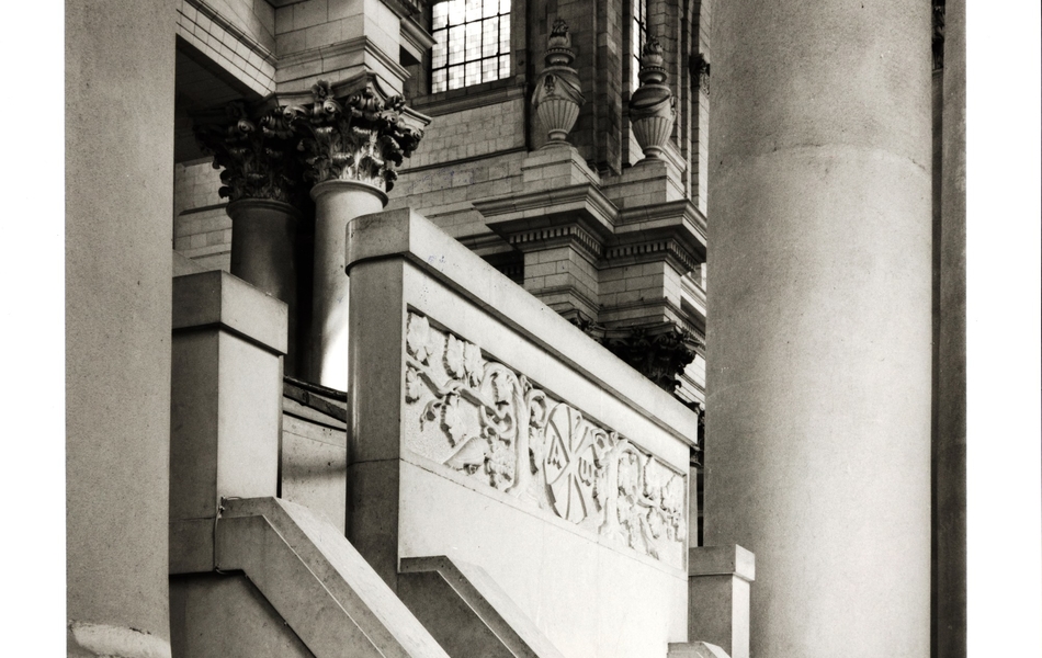 Photographie noir et blanc montrant un escalier massif ouvragé, encadré de colonnes de pierre sculptées.
