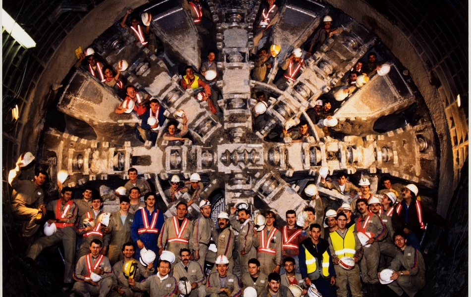 Photographie couleur montrant un groupe d'hommes posant devant et derrière une énorme matrice de chantier.