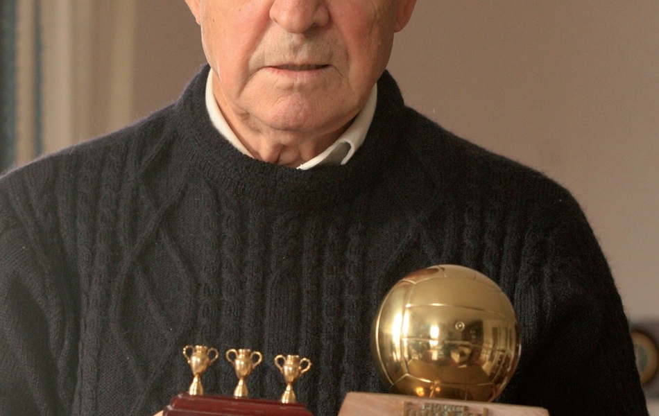 Photographie couleur montrant un homme âgé tenant deux trophées.